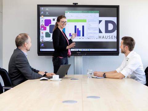 Drei Mitarbeitende bei einer Präsentation in einem Konferenzsaal